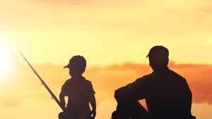 L'immagine mostra la silhouette di un adulto e di un bambino con una canna da pesca in mano, immersi nella luce calda di un tramonto vicino a uno specchio d'acqua
