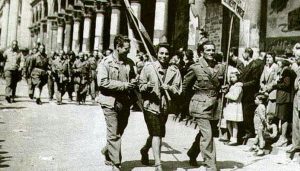 L'immagine mostra la celebre sfilata dei partigiani a Milano durante le giornate della Liberazione nel maggio del 1945, con la partigiana Eva Colombo al centro che regge la bandiera del Comando dell'Oltrepò Pavese