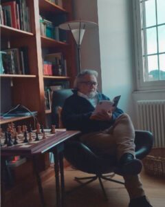 foto di flavio lucibello seduto mentre legge un libro e si trova accanto ad un tavolo con degli scacchi